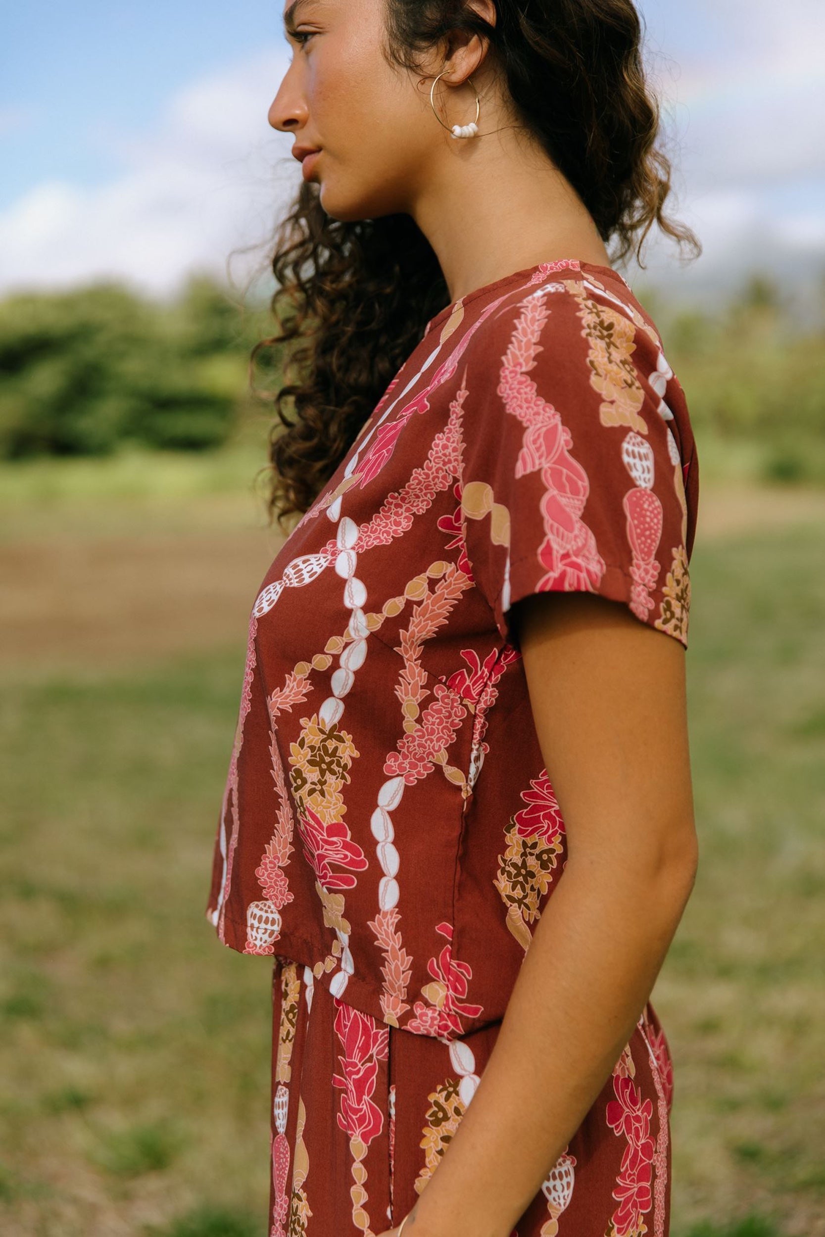 woman with brown hair wearing red-brown colored top with button closure back and lei print