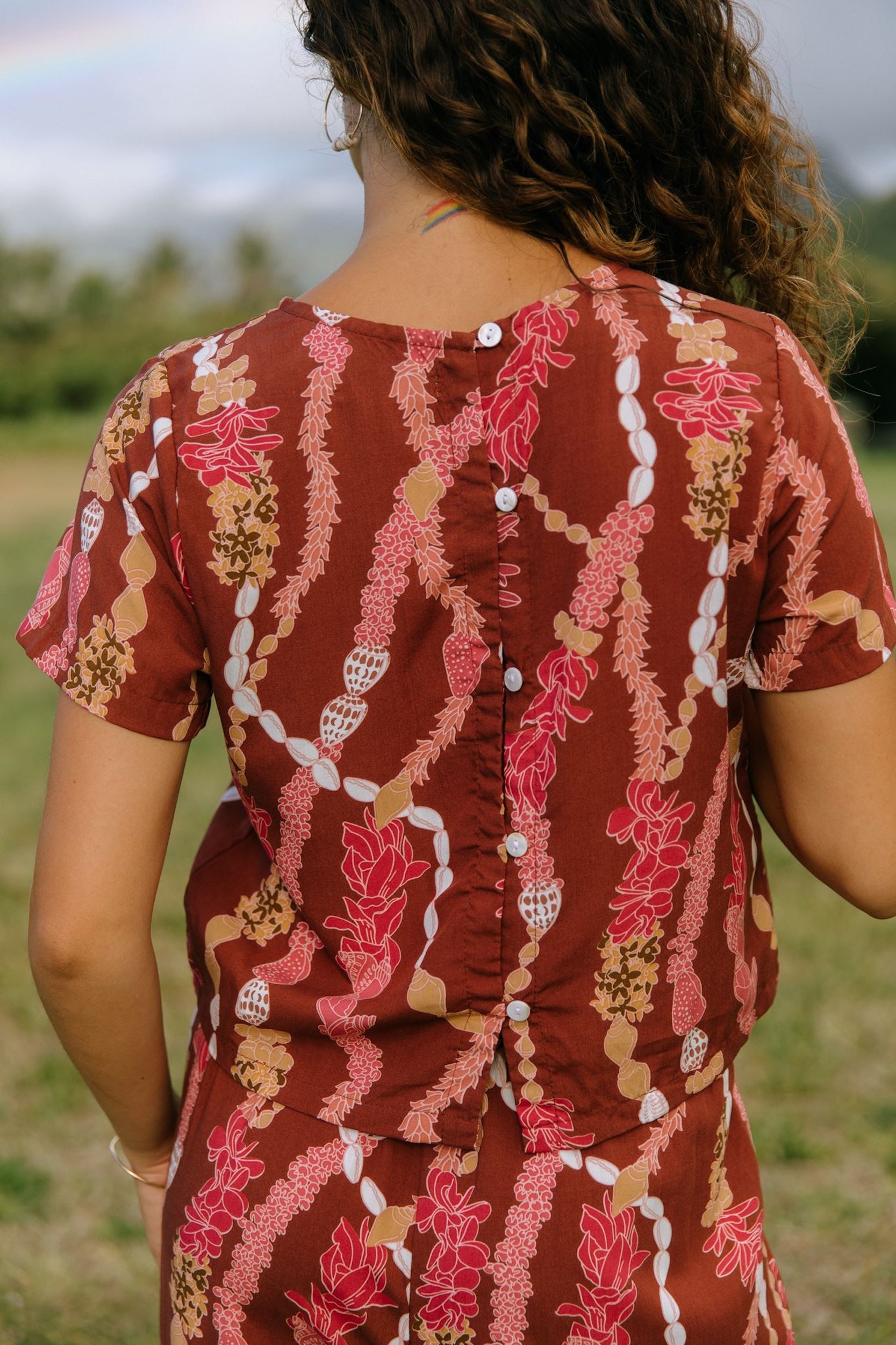woman with brown hair wearing red-brown colored top with button closure back and lei print