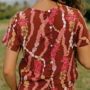 woman with brown hair wearing red-brown colored top with button closure back and lei print