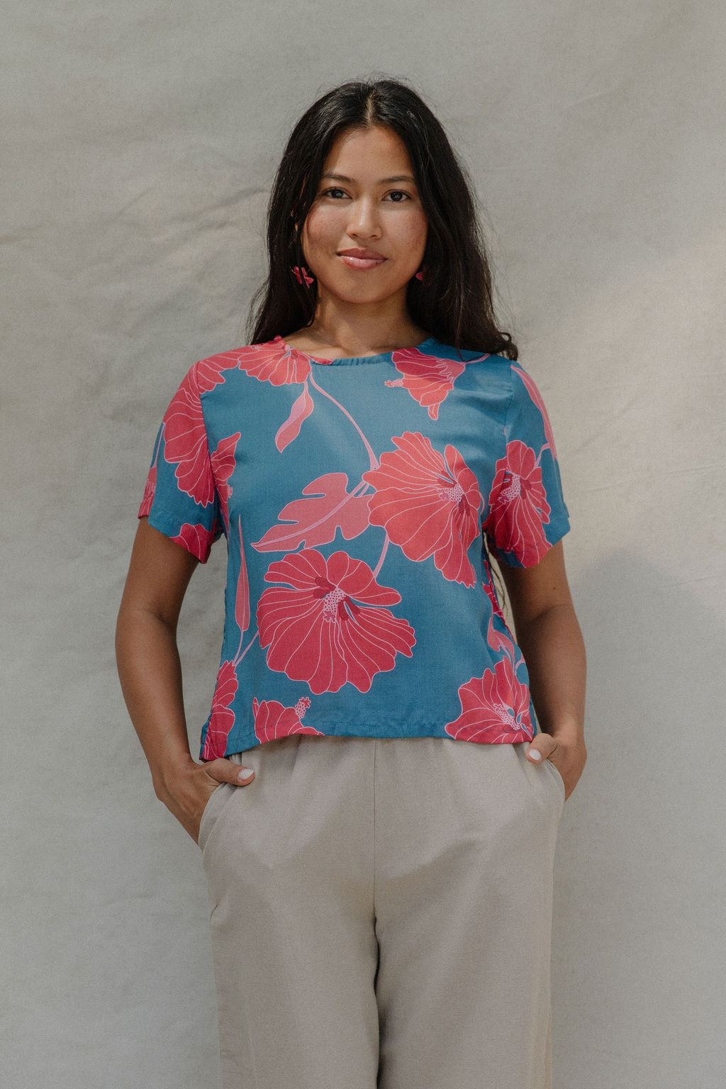 woman with brown hair wearing a aqua blue shirt with button up back with red mao flower pattern