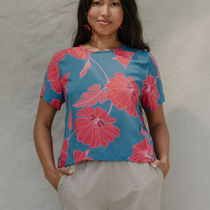woman with brown hair wearing a aqua blue shirt with button up back with red mao flower pattern