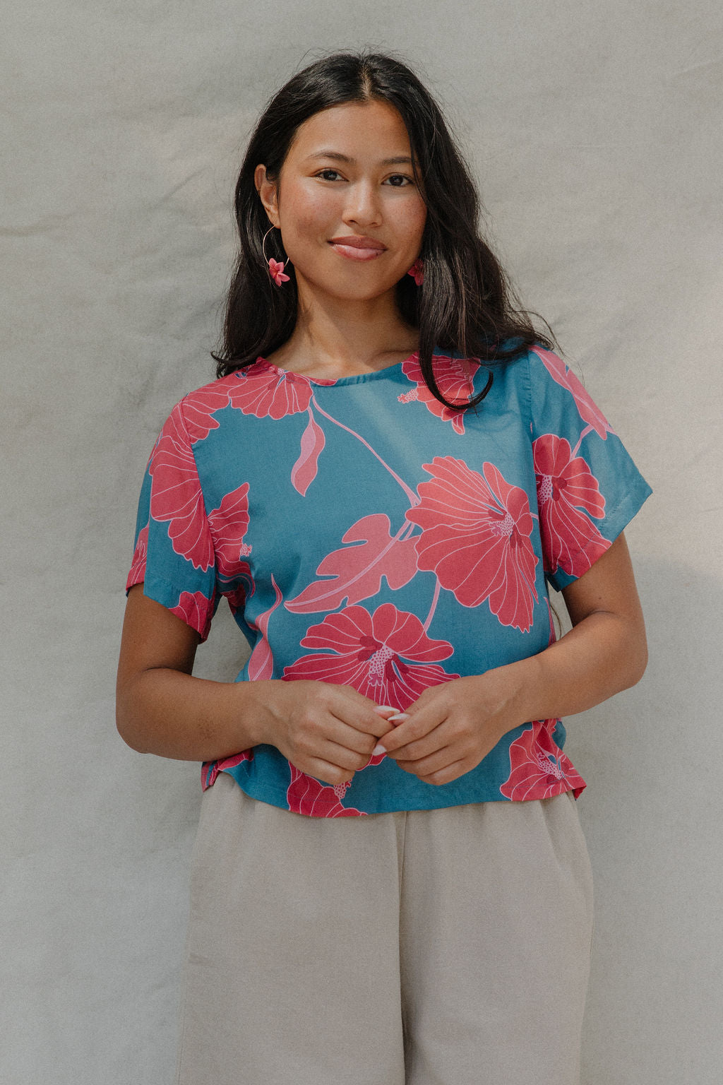 woman with brown hair wearing a aqua blue shirt with button up back with red mao flower pattern