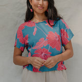 woman with brown hair wearing a aqua blue shirt with button up back with red mao flower pattern
