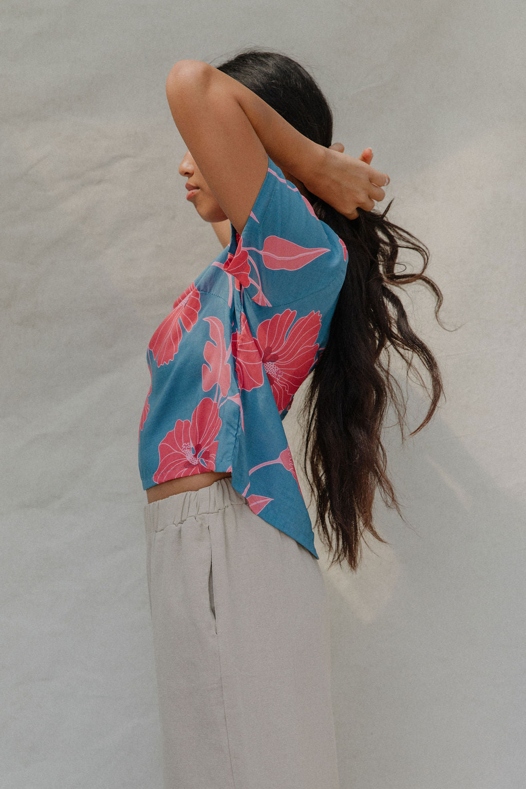 woman with brown hair wearing a aqua blue shirt with button up back with red mao flower pattern