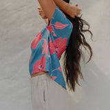 woman with brown hair wearing a aqua blue shirt with button up back with red mao flower pattern