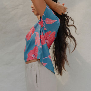 woman with brown hair wearing a aqua blue shirt with button up back with red mao flower pattern