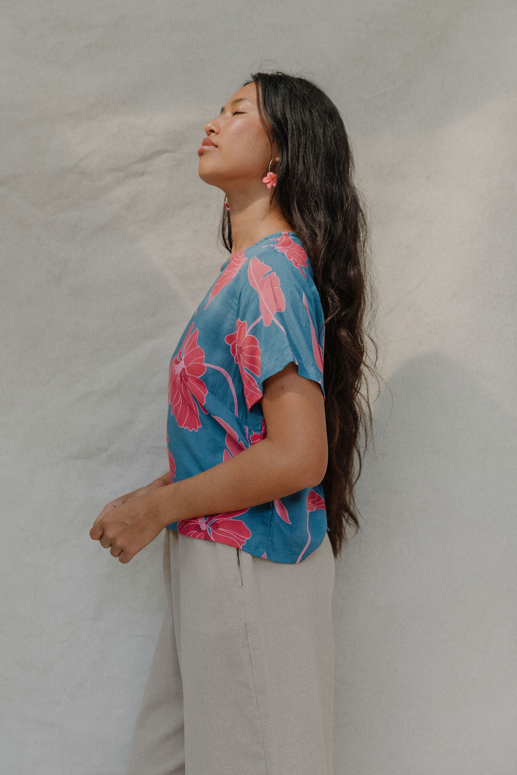 woman with brown hair wearing a aqua blue shirt with button up back with red mao flower pattern