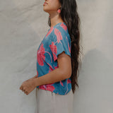 woman with brown hair wearing a aqua blue shirt with button up back with red mao flower pattern