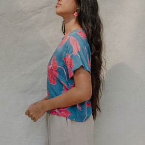 woman with brown hair wearing a aqua blue shirt with button up back with red mao flower pattern