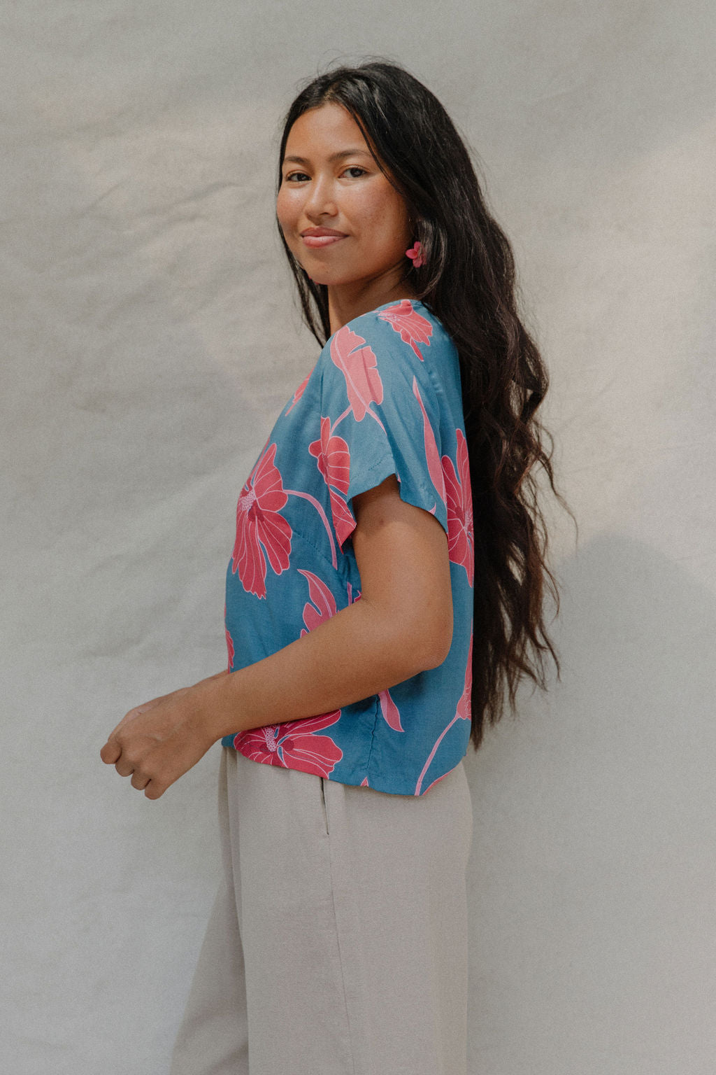 woman with brown hair wearing a aqua blue shirt with button up back with red mao flower pattern