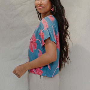 woman with brown hair wearing a aqua blue shirt with button up back with red mao flower pattern