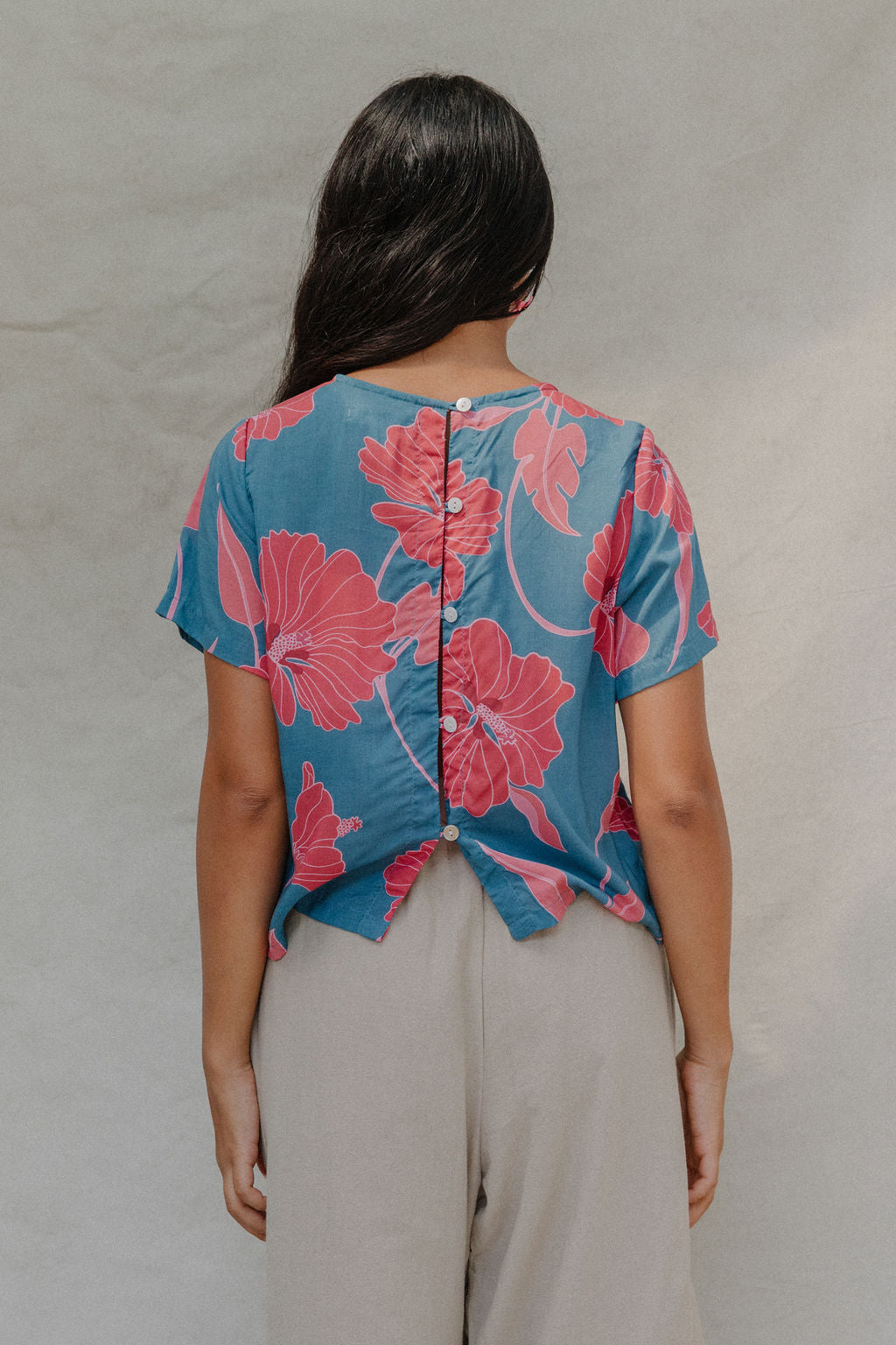 woman with brown hair wearing a aqua blue shirt with button up back with red mao flower pattern