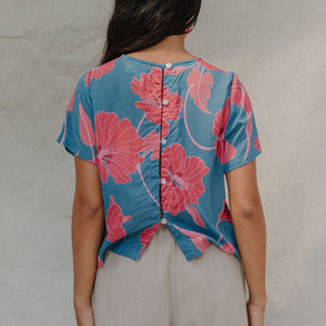 woman with brown hair wearing a aqua blue shirt with button up back with red mao flower pattern
