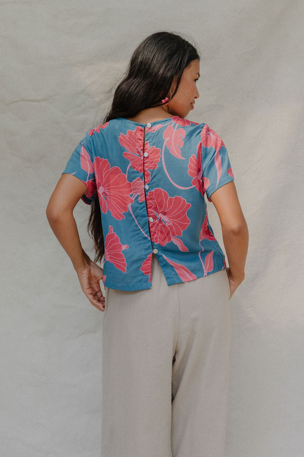 woman with brown hair wearing a aqua blue shirt with button up back with red mao flower pattern