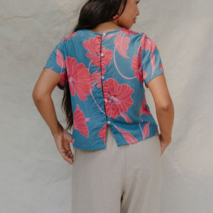 woman with brown hair wearing a aqua blue shirt with button up back with red mao flower pattern
