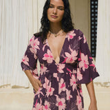 woman wearing dark purple playsuit with half sleeve, plunging neck line, pockets in an orchid print
