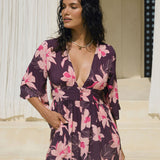 woman wearing dark purple playsuit with half sleeve, plunging neck line, pockets in an orchid print