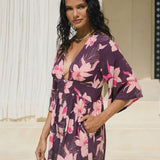 woman wearing dark purple playsuit with half sleeve, plunging neck line, pockets in an orchid print
