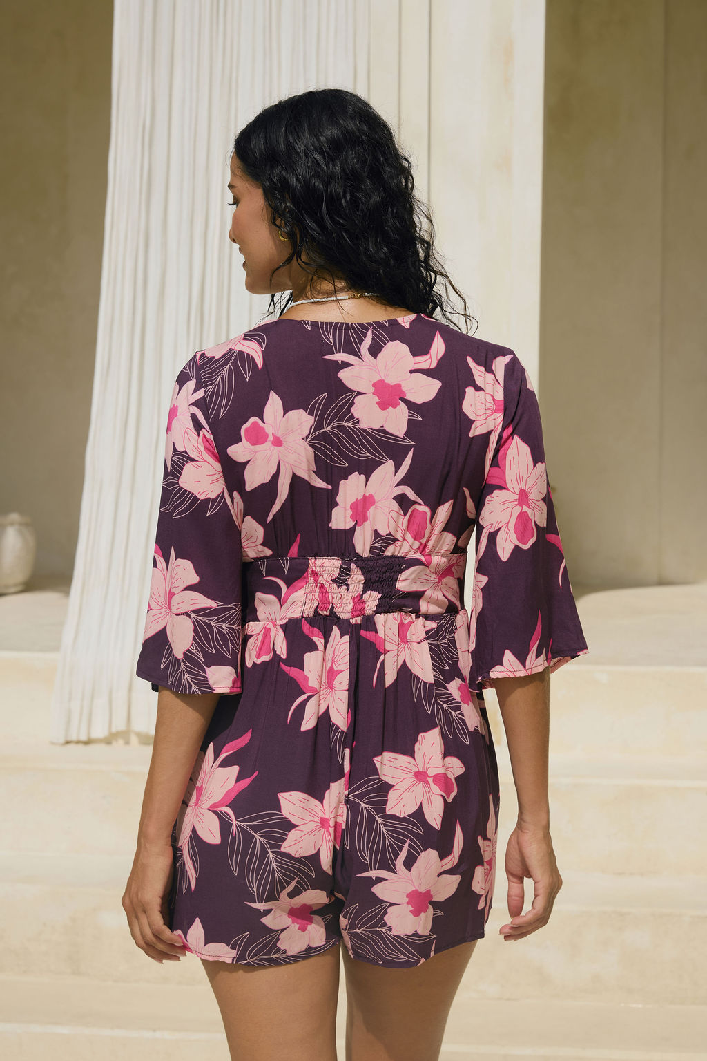 woman wearing dark purple playsuit with half sleeve, plunging neck line, pockets in an orchid print