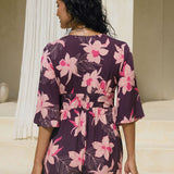woman wearing dark purple playsuit with half sleeve, plunging neck line, pockets in an orchid print