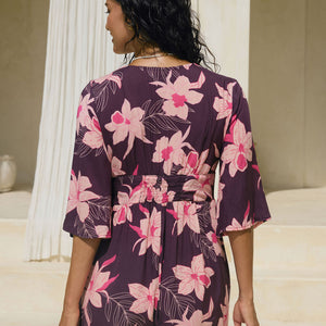 woman wearing dark purple playsuit with half sleeve, plunging neck line, pockets in an orchid print