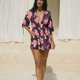 woman wearing dark purple playsuit with half sleeve, plunging neck line, pockets in an orchid print