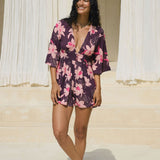 woman wearing dark purple playsuit with half sleeve, plunging neck line, pockets in an orchid print