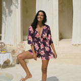 woman wearing dark purple playsuit with half sleeve, plunging neck line, pockets in an orchid print