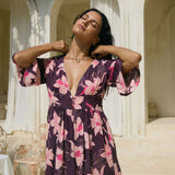 woman wearing dark purple playsuit with half sleeve, plunging neck line, pockets in an orchid print