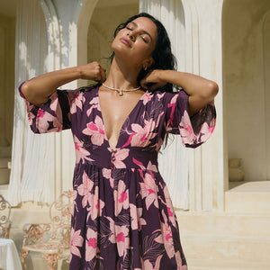 woman wearing dark purple playsuit with half sleeve, plunging neck line, pockets in an orchid print