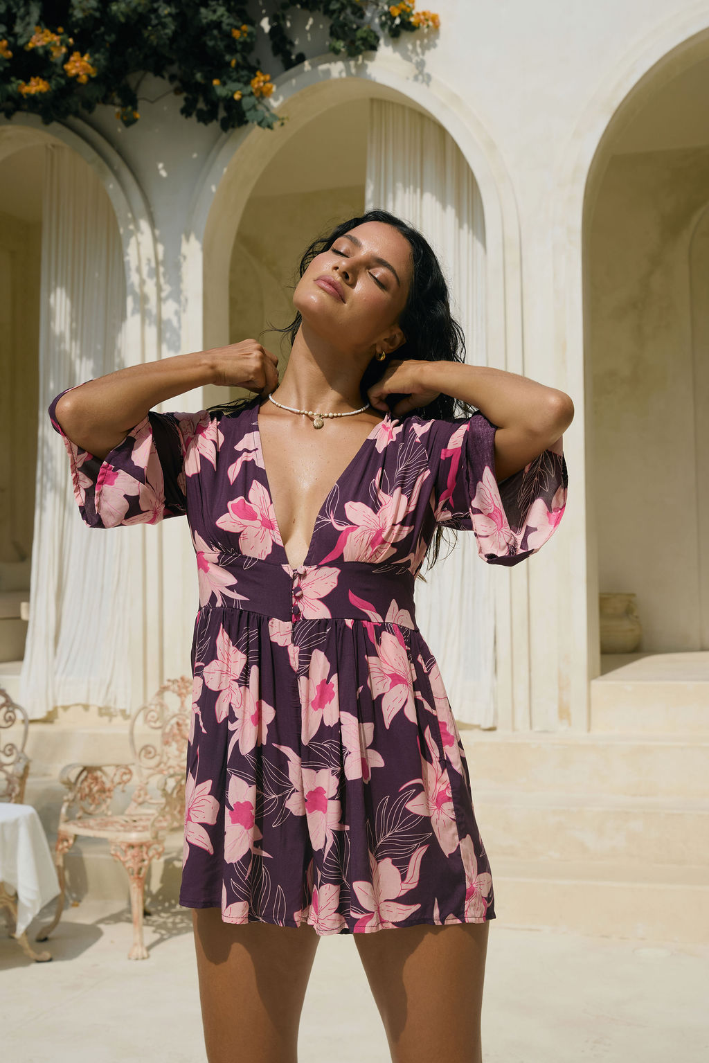 woman wearing dark purple playsuit with half sleeve, plunging neck line, pockets in an orchid print