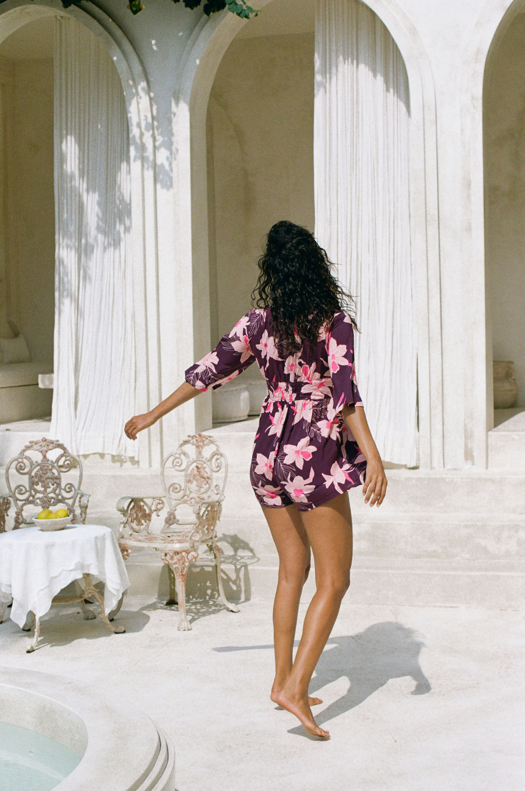 woman wearing dark purple playsuit with half sleeve, plunging neck line, pockets in an orchid print