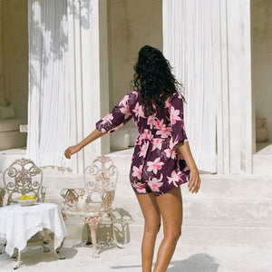 woman wearing dark purple playsuit with half sleeve, plunging neck line, pockets in an orchid print
