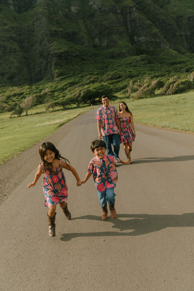 little girl wearing a navy spaghetti strap dress with bright pink hibiscus print