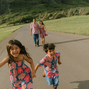 little boy wearing a nevy button up aloha shirt with bright pink hibiscus print