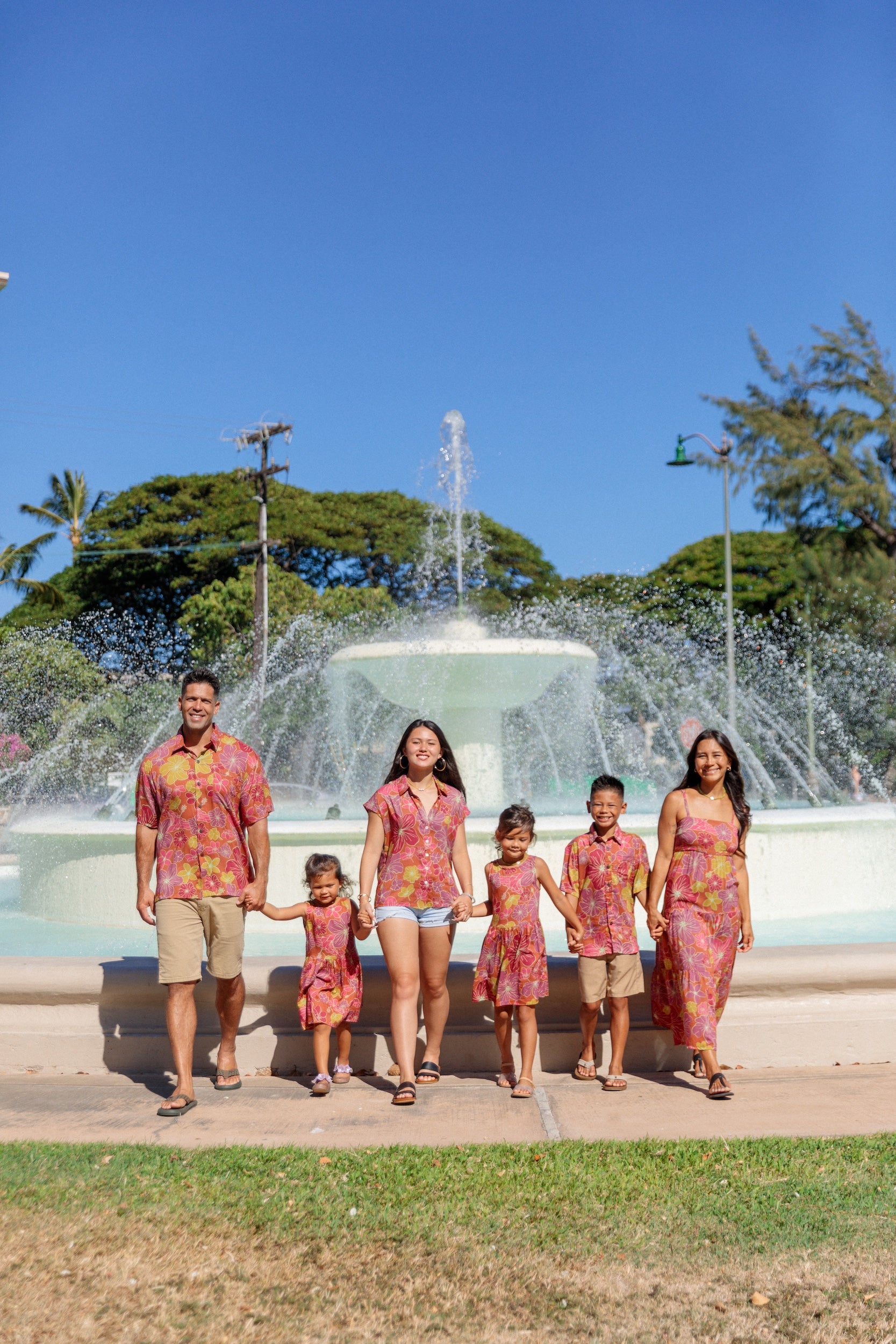 little boy wearing terracotta colored aloha shirt with large purple and yellow flower print 