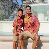 little boy wearing terracotta colored aloha shirt with large purple and yellow flower print 