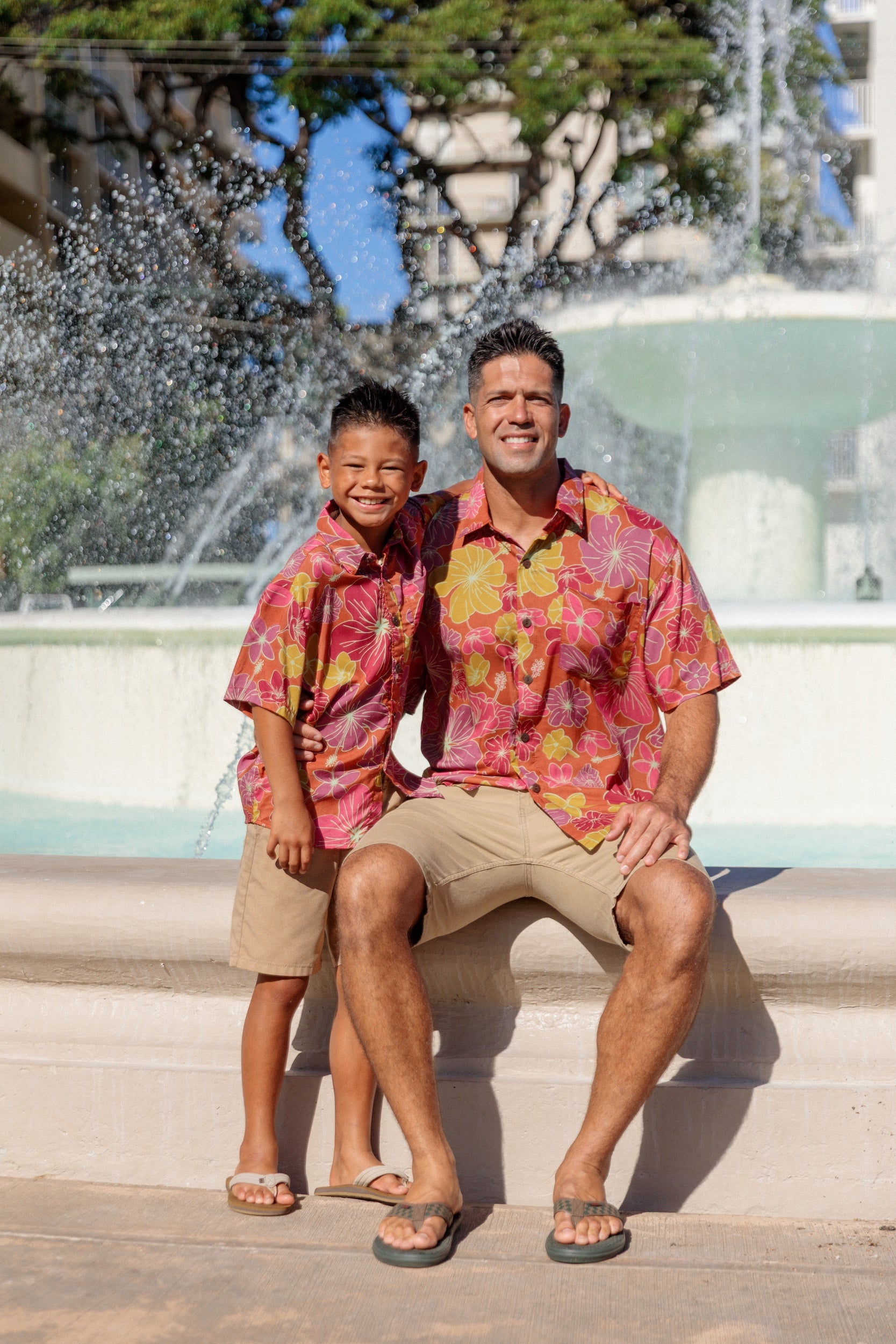 little boy wearing terracotta colored aloha shirt with large purple and yellow flower print 