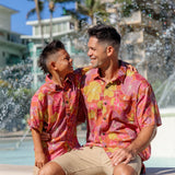 man wearing terracotta colored aloha shirt with large purple and yellow flower print