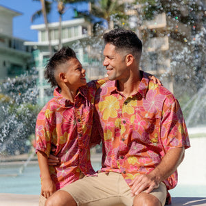 man wearing terracotta colored aloha shirt with large purple and yellow flower print