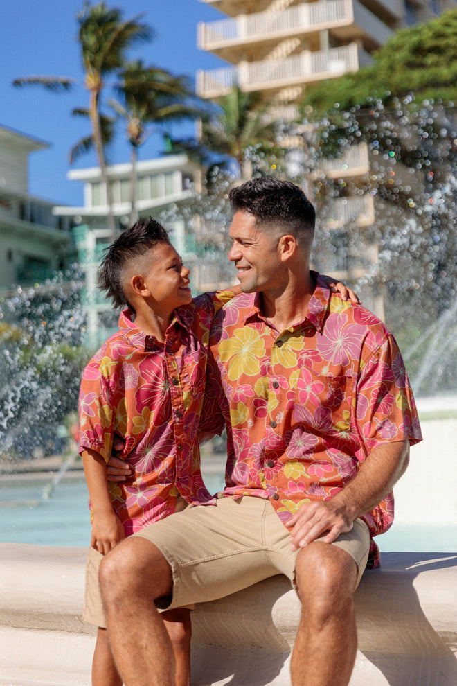 man wearing terracotta colored aloha shirt with large purple and yellow flower print