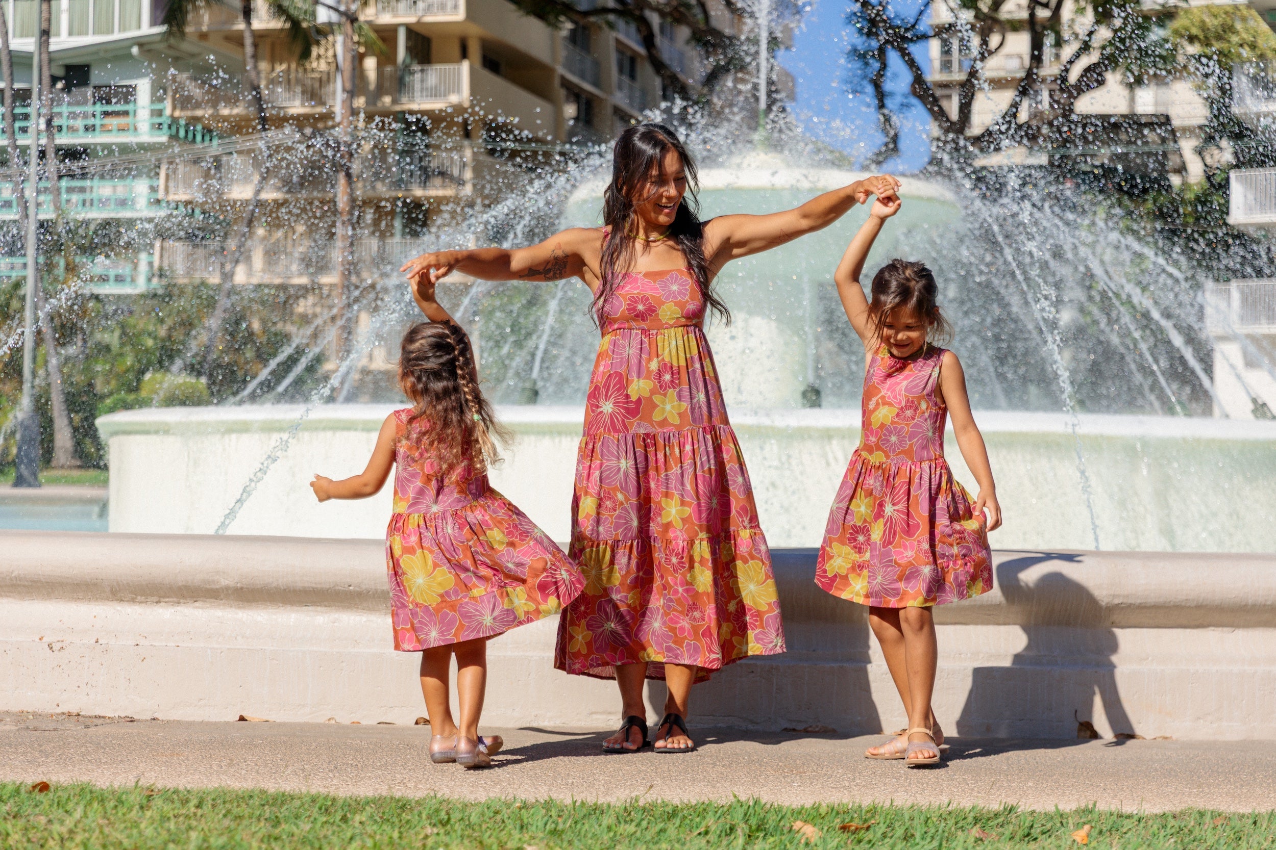 little girl wearing terracotta colored high neck sleeveless knee length dress with large purple and yellow flower print