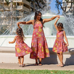 little girl wearing terracotta colored high neck sleeveless knee length dress with large purple and yellow flower print