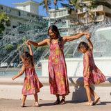 little girl wearing terracotta colored high neck sleeveless knee length dress with large purple and yellow flower print