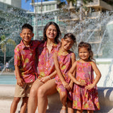 little boy wearing terracotta colored aloha shirt with large purple and yellow flower print 