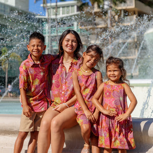 little boy wearing terracotta colored aloha shirt with large purple and yellow flower print 