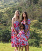 little girl with brown hair wearing a mid length dress with periwinkle background and bright red hibiscus print.