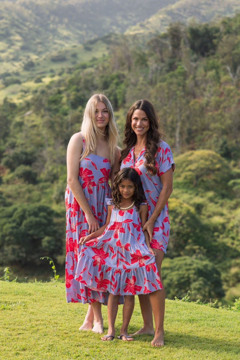 little girl with brown hair wearing a mid length dress with periwinkle background and bright red hibiscus print.