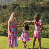 little girl with brown hair wearing a mid length dress with periwinkle background and bright red hibiscus print.