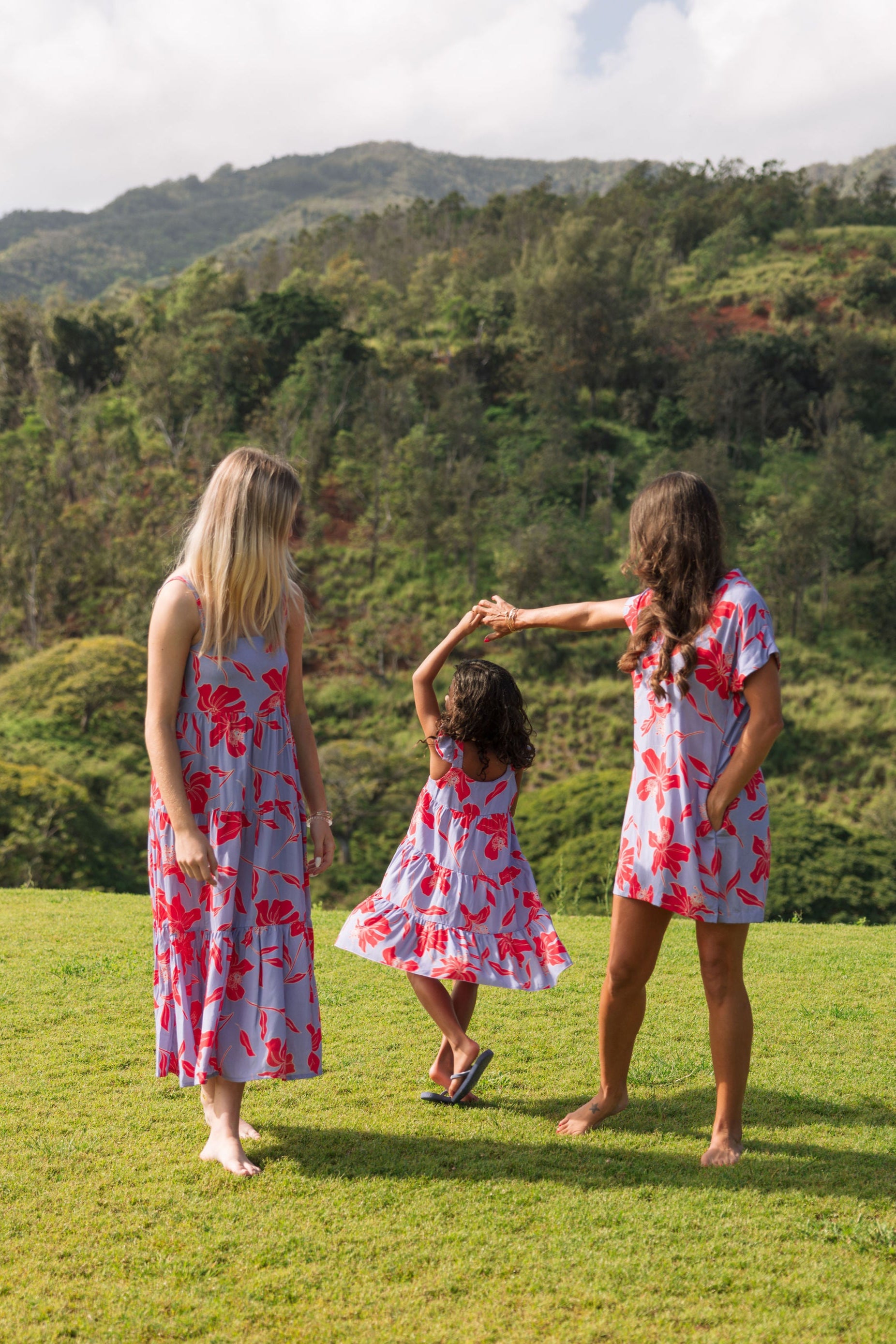 little girl with brown hair wearing a mid length dress with periwinkle background and bright red hibiscus print.